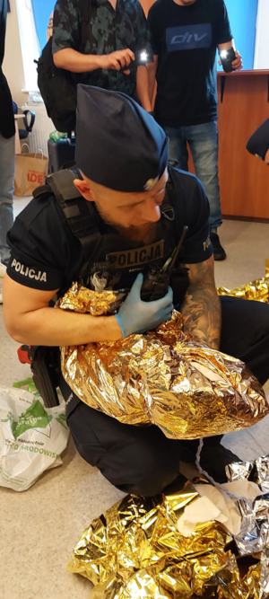 policjant trzyma koc termiczny i krótkofalówkę w drugiej ręce